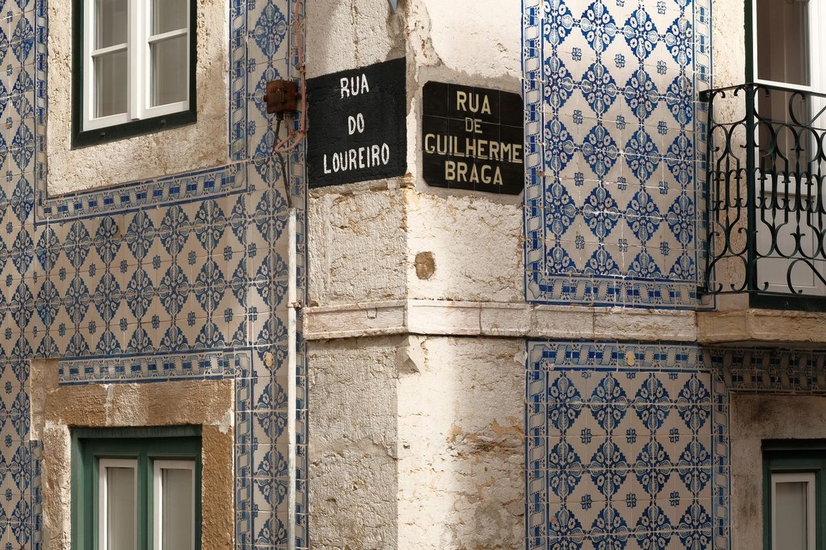A Lisbon house front covered in blue and white azulejo tiles with street name plaques on the corner, the registered home address behind a Portuguese NIF record
