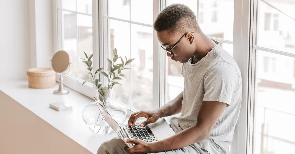 A man applying online from home on a laptop by a bright window, the starting point for getting a Portuguese NIF without a fiscal representative where the law allows it