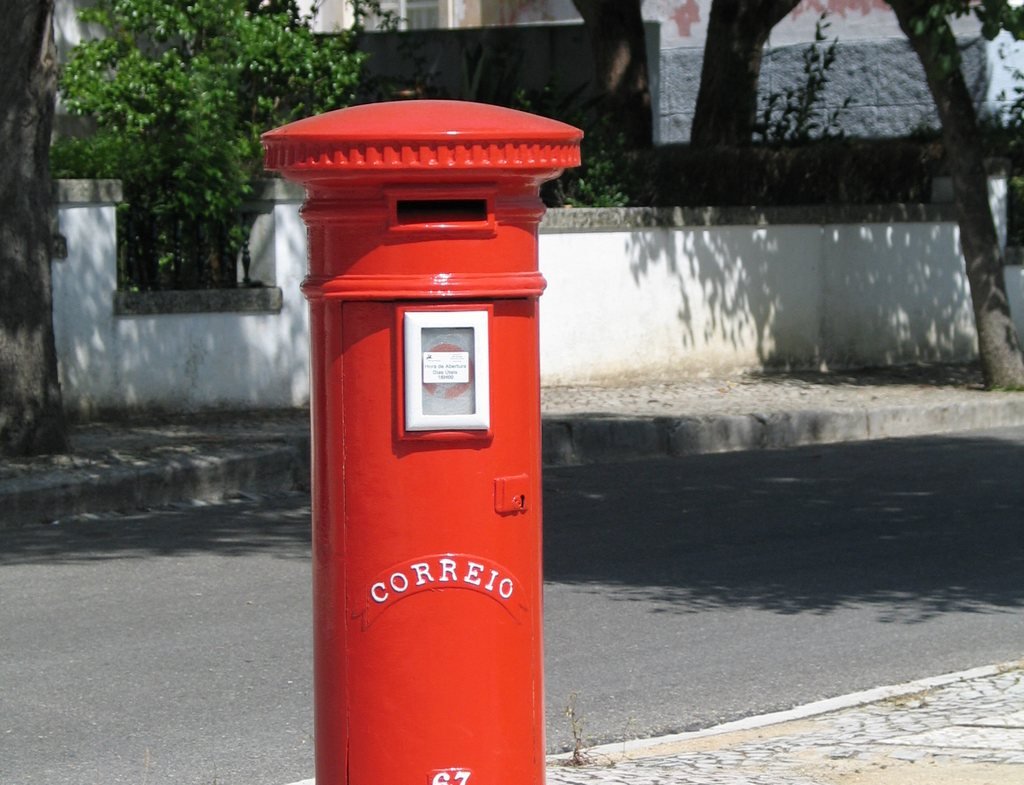 A red CTT pillar post box on a pavement in Portugal, the postal service that delivers the Finanças password letter