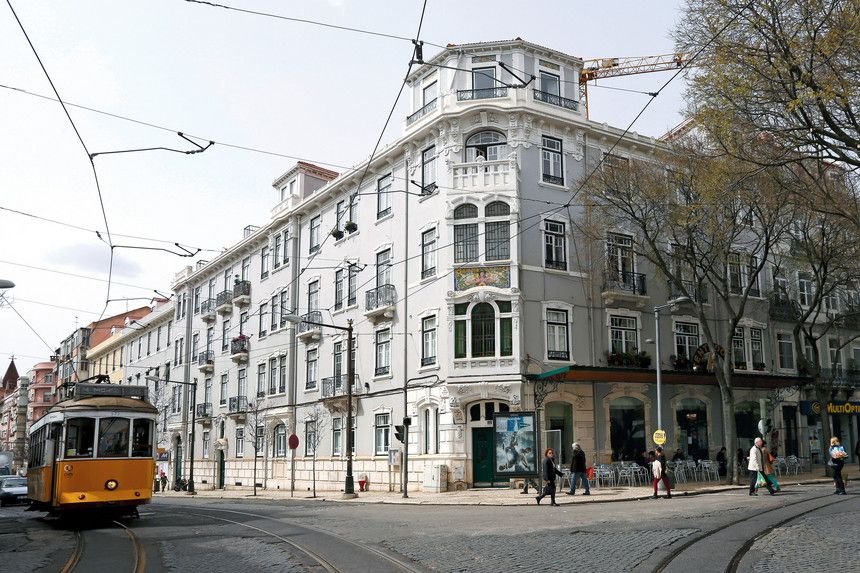 A residential street in Campo de Ourique, Lisbon, Portugal, with a yellow tram passing apartment buildings where new residents register their Portuguese home address