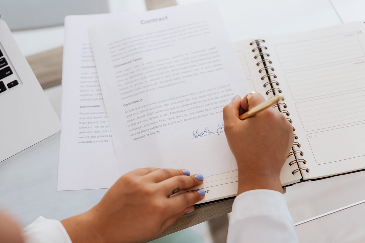 A seller's hand signing a sale contract document with a pen, the escritura signing moment when a Portuguese property sale completes