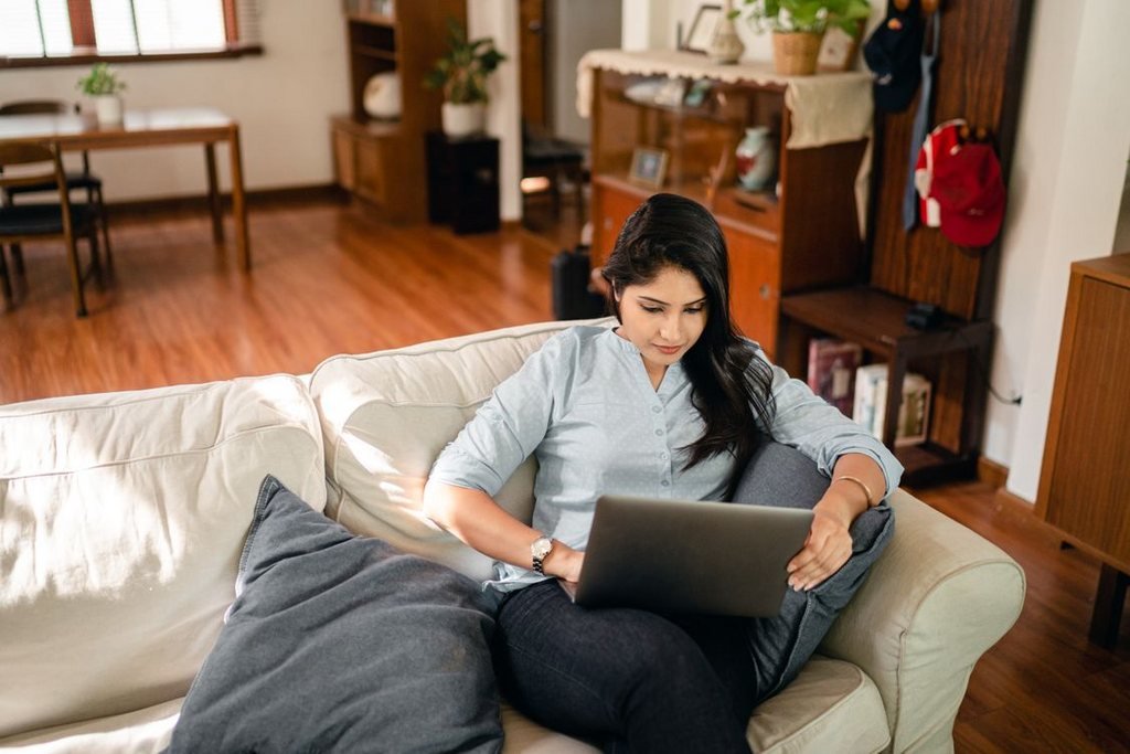 A woman on her sofa at home applying online with a laptop, the remote way to get a Portuguese NIF without visiting a tax office