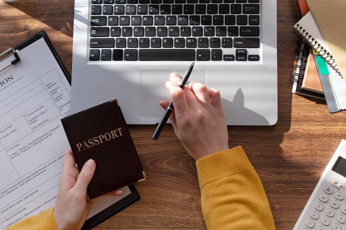 Hands holding a passport beside a visa application form and a laptop on a desk, the documents a D7 visa file is built from