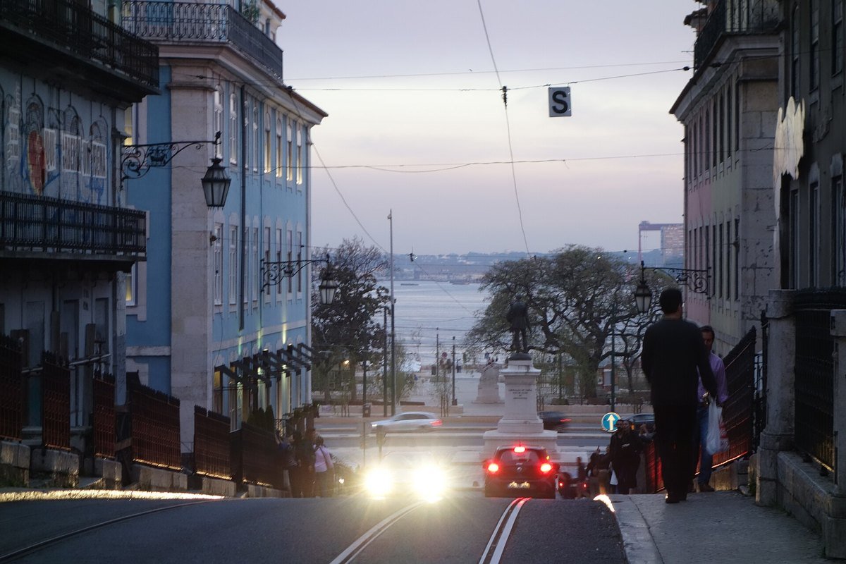 Rua do Alecrim in Lisbon at dusk, a quiet street of older houses sloping down towards the Tagus river