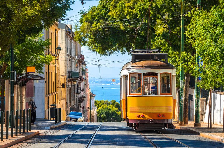 Yellow Lisbon tram climbing a sunny street towards the Tagus river